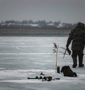 man ice fishing on a lake